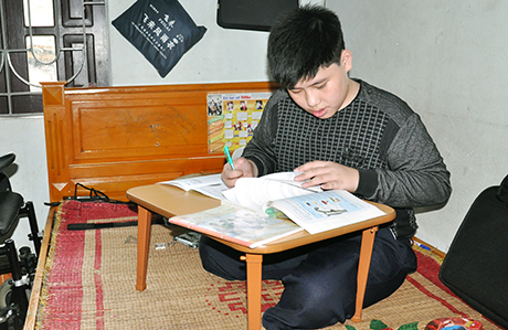 Nhờ có sự giúp đỡ của các tổ chức, cá nhân, em Nguyễn Xuân Ngọc có điều kiện tốt để đến trường. (Trong ảnh: Ngọc đang học bài, bên giường là chiếc xe lăn điện gia đình mua cho Ngọc bằng tiền ủng hộ của các nhà hảo tâm).