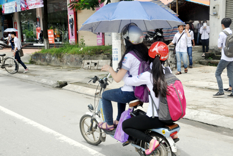 Trên đường Nguyễn Văn Cừ, học sinh cầm ô che nắng khi đi xe, không đảm bảo ATGT.