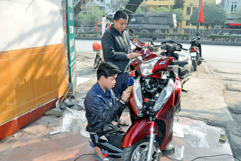 Anh Bùi Quang Quyền hướng dẫn Nguyễn Văn Đỗ (người ngồi) bọc dán xe máy.