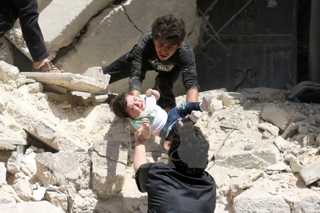 Chuyển một em bé khỏi đống đổ nát sau vụ không kích ở thành phố Aleppo ngày 28/4. (Nguồn: AFP/TTXVN)