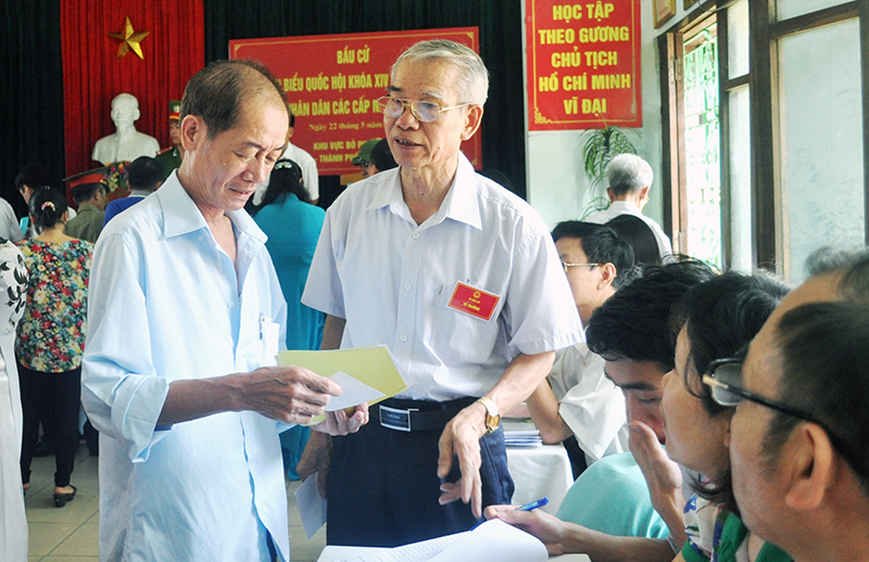 Ông Nguyễn Xuân Tín, Tổ trưởng Tổ bầu cử số 3 (bên phải) hướng dẫn cử tri khu phố 3, phường Hồng Hà (TP Hạ Long) nhận phiếu bầu trong ngày bầu cử 22-5.