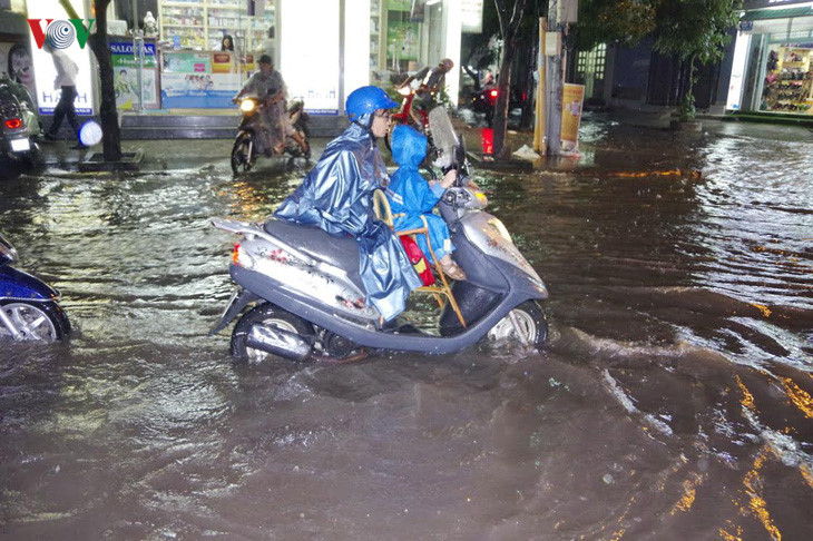   Người mẹ dắt xe chở con lội trong nước giữa cơn mưa lớn.