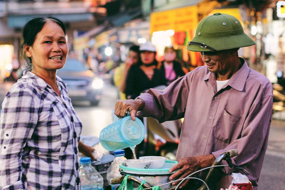 Cặp vợ chồng bán tào phớ rong trên phố cổ với thu nhập 100.000 – 150.000 đồng/ngày. (Ảnh: Thanh Dung/Vietnam+) 