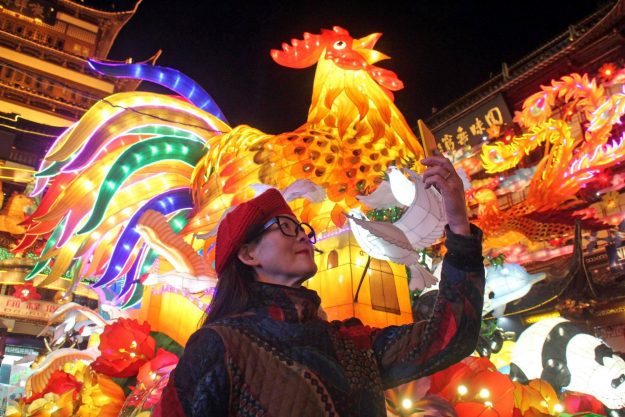 Một phụ nữ chụp ảnh cùng đèn lồng có hình gà trống tại thành phố Thượng Hải, Trung Quốc (Ảnh: China Daily)