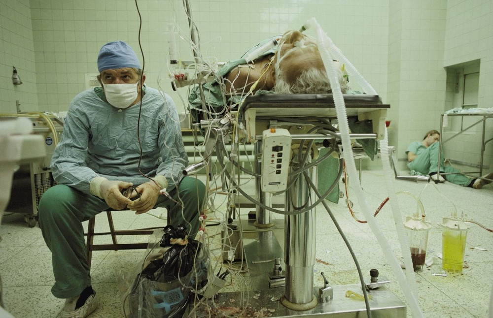 GS Zbigniew Religa (1938-2009) - người tiên phong trong lĩnh vực phẫu thuật cấy ghép tim tại Ba Lan - ngồi trầm ngâm sau ca phẫu thuật thành công kéo dài 23 giờ. Trong khi đó, trợ lý của ông ngủ gục ở góc phòng vì kiệt sức. Ảnh: J. Steinfeld/National Geographic 1987.