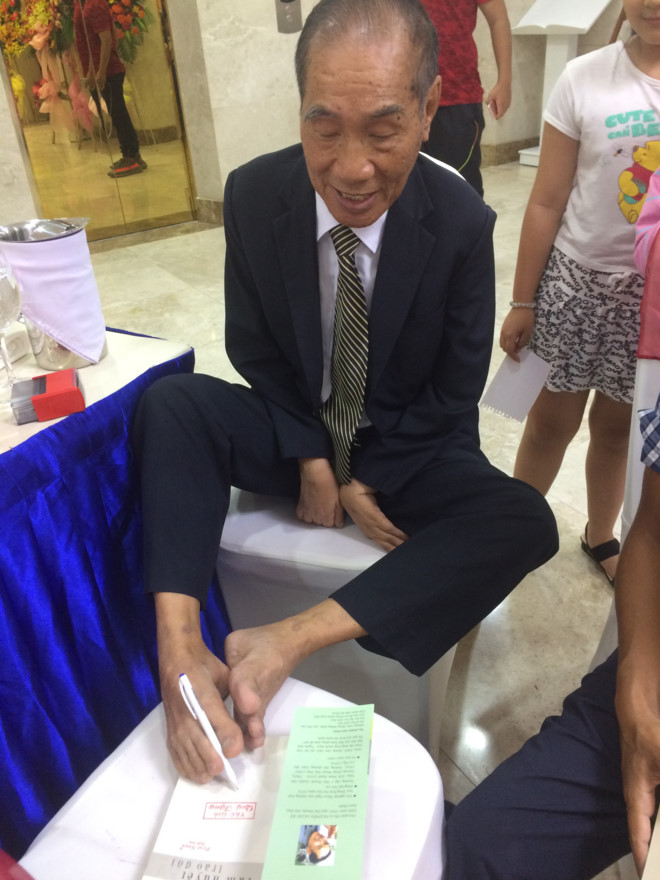 Thầy giáo Nguyễn Ngọc Ký ký tặng sách bằng chân. Ảnh: Trí Việt.