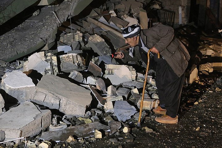 Một người đàn ông Iraq cao tuổi dùng đèn pin để soi qua đống đổ nát của một tòa nhà ở quận Derbendihan thuộc thành phố Sulaymaniyah. Ảnh: Getty.