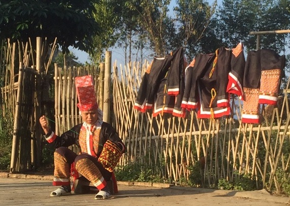 Một phụ nữ Dao Thanh Phán vừa thêu vừa phơi những bộ trang phục dân tộc.