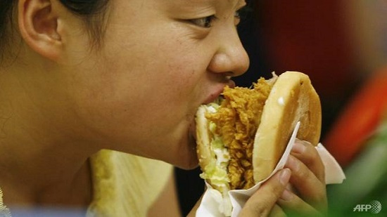 Một người phụ nữ ăn burger trong một cửa hàng đồ ăn nhanh ở Bắc Kinh. Ảnh: AFP
