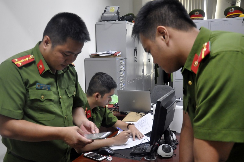 Đại úy Phú (trái) hướng dẫn đồng nghiệp tra tìm thông tin qua điện thoại của nạn nhân để phục vụ công tác điều tra vụ án.