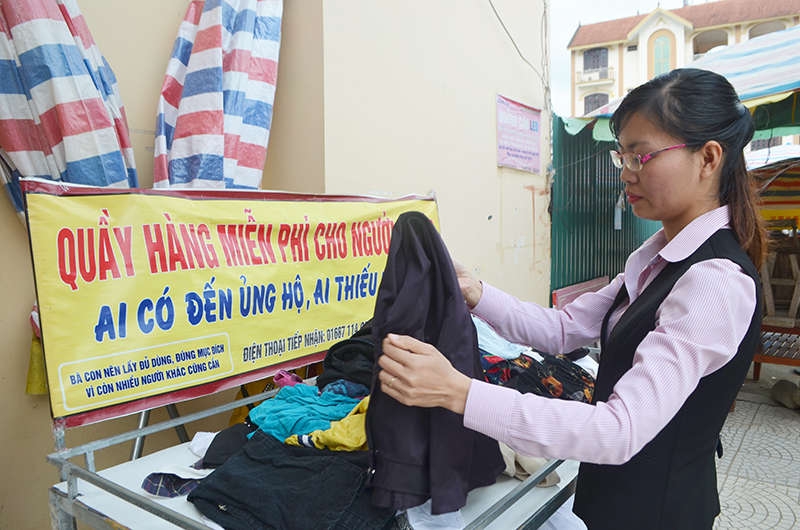 Chị Nhung gấp quần áo tại quầy hàng miễn phí đặt trước trụ sở Ngân hành Chính sách xã hội huyện Bình Liêu