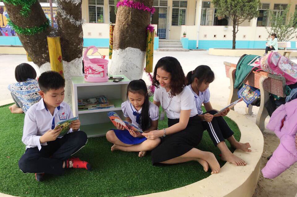 Cô và trò Trường Tiểu học Hạ Long 1 (huyện Vân Đồn) đọc sách ngoài sân trường.