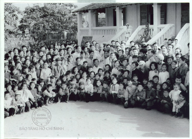  Chủ tịch Hồ Chí Minh chụp ảnh lưu niệm cùng cô và trò Trường Cấp I, II Móng Cái. Người đứng giáp tay trái Bác là cô giáo Hoàng Kim Điệp