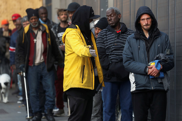 Một nhân viên đeo khẩu trang hướng dẫn người vô gia cư nhận cơm miễn phí tại California, Mỹ - Ảnh: REUTERS