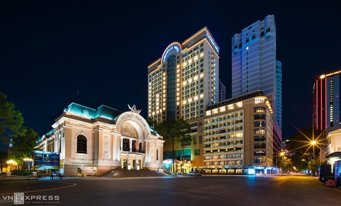 Quảng trường Nhà hát Thành phố (trái) và Khánh sạn Caravelle 5 sao lung linh ánh đèn khi về đêm 3/4, bên ngoài là 2 người bảo vệ trực. Trên đường phố, không một bóng người qua lại. 