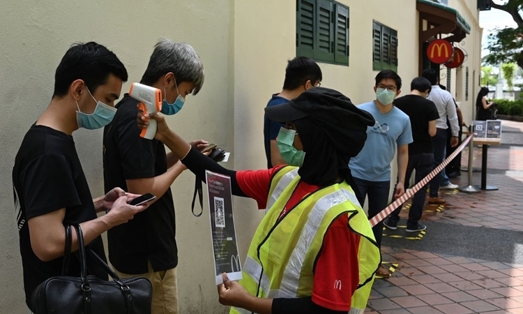 Nhân viên tiệm ăn nhanh McDonald đo thân nhiệt khách hàng trong ngày mở cửa trở lại hôm 11/5 tại Singapore. Ảnh: AFP.