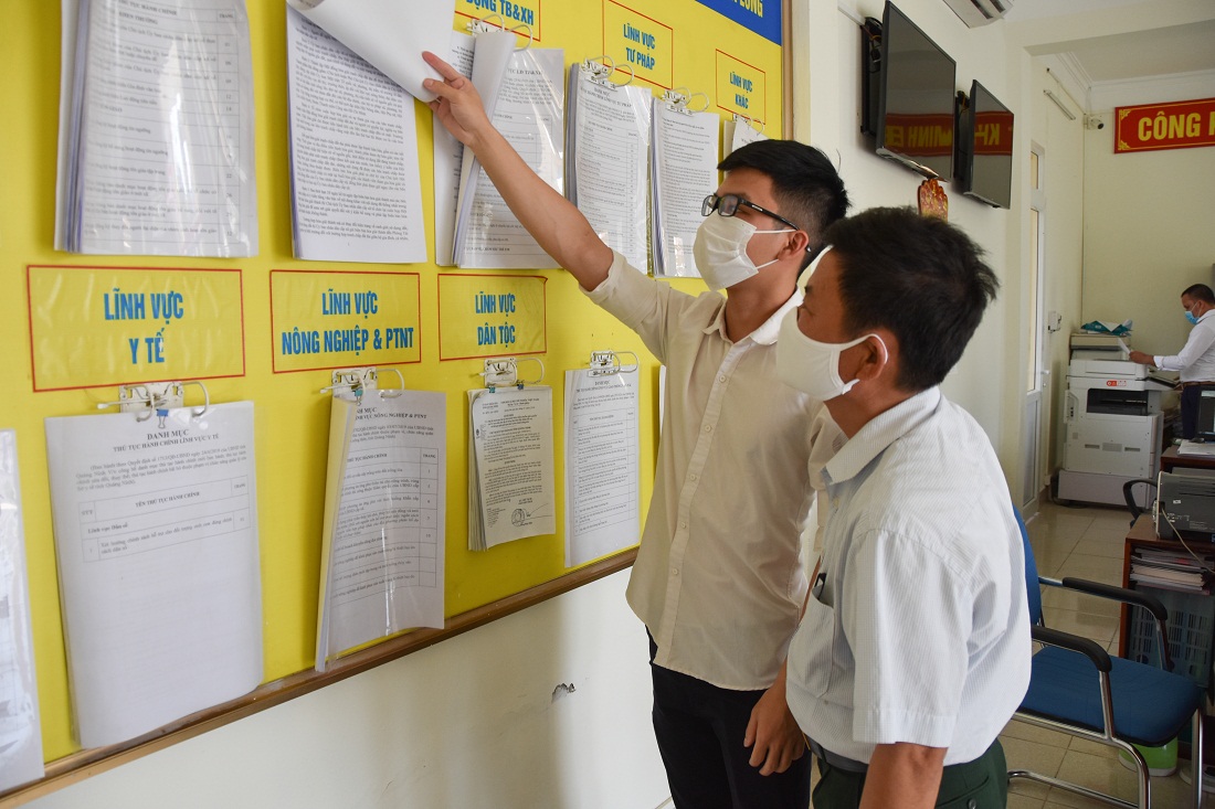 Cán bộ phường Ka Long (TP Móng Cái) hướng dẫn người dân theo dõi các nội dung niêm yết công khai tại trụ ở UBND phường, bao gồm nội dung về kết quả bình xét, rà soát hộ nghèo, cận nghèo.
