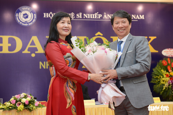 Cựu chủ tịch Hội Nghệ sĩ nhiếp ảnh Việt Nam Vũ Quốc Khánh tặng hoa chúc mừng tân chủ tịch Trần Thị Thu Đông - Ảnh: ĐỖ NHUNG