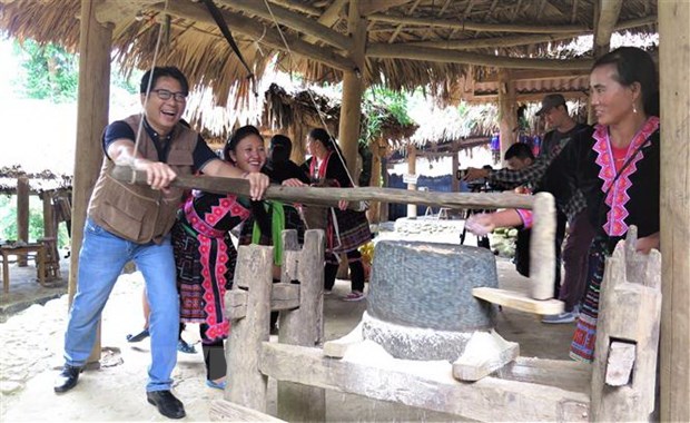 Du khách cùng người dân bản Sin Suối Hồ trải nghiệm hoạt động xay ngô. (Ảnh: Việt Hoàng/TTXVN)