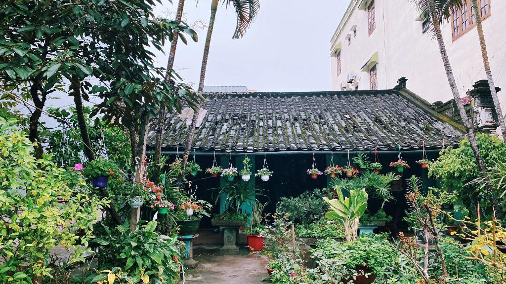 Căn nhà cổ với mái tam sơn và hai trụ biểu nằm giwuax một vườn hoa lá.