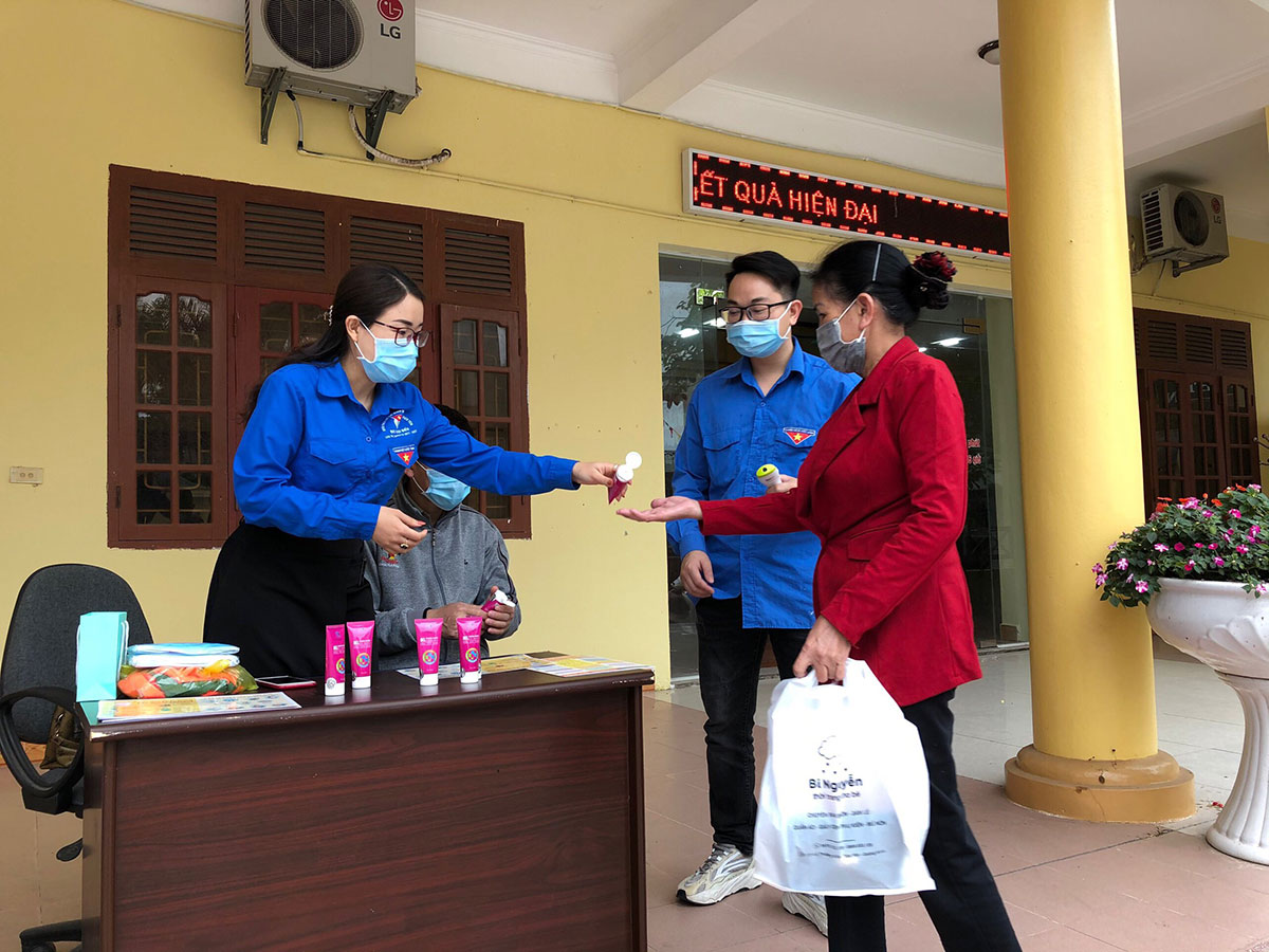 Chi Mai Việt Hồng (bên trái) đang hướng dẫn người dân sử dụng nước sát khuẩn phòng chống dịch Covid-19. 