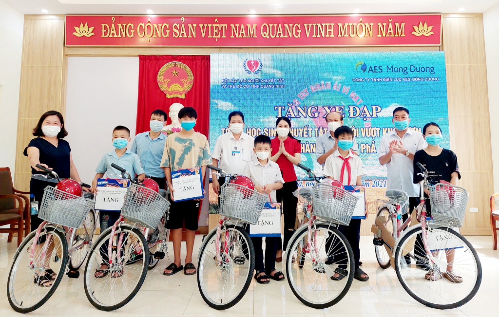 Đại diện Hội Bảo trợ NKT-TMC tỉnh và Công ty TNHH Điện lực AES Mông Dương trao tặng xe đạp và mũ bảo hiểm cho học sinh mô côi, khuyết tật  vượt khó khăn lên. 