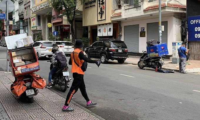 Delivery workers for e-commerce platforms Shopee (orange) and Lazada (blue) wait for customers on Cao Ba Quat Road in HCMC’s District 1, Nov. 16, 2021. 