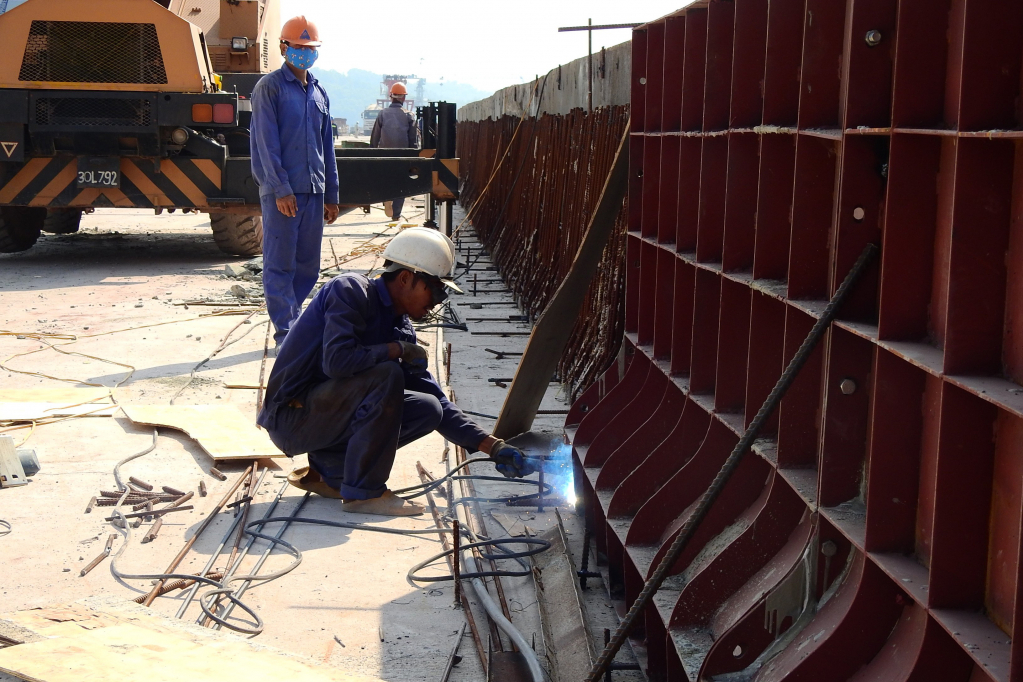 Workers are constructing the median strip and the guardrail on both sides of the bridge.