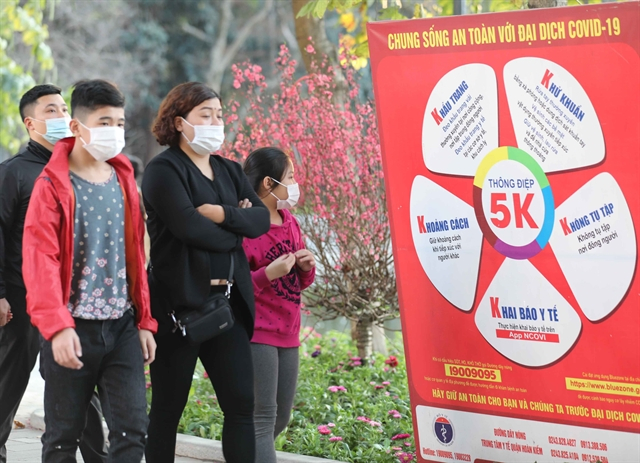 A family in Hà Nội passed by a Health Ministry's 5K message panel in Hoàn Kiếm Lake area during Tết (Lunar New Year) holiday of 2021. The health ministry has proposed stopping all entertainment activities during the coming Tết holidays.