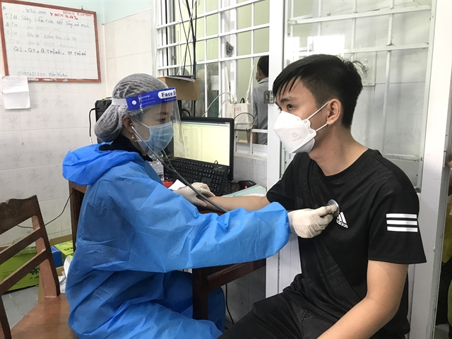 A medical worker examines a man before giving the booster dose of COVID-19 vaccine in the Mekong Delta province of Vĩnh Long.