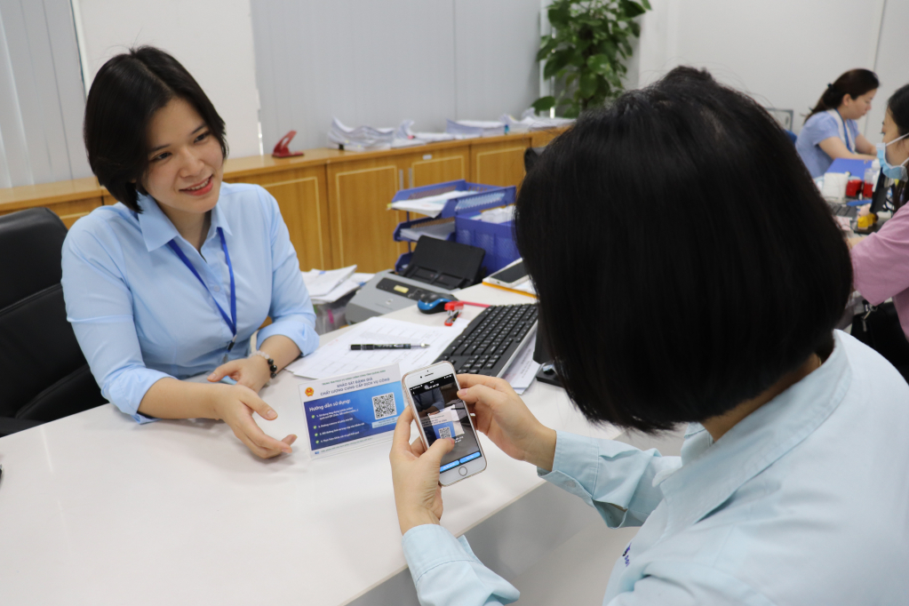 Chị Nguyễn Ngọc Yến hướng dẫn người dân quét mã QR để đánh giá chất lượng dịch vụ.