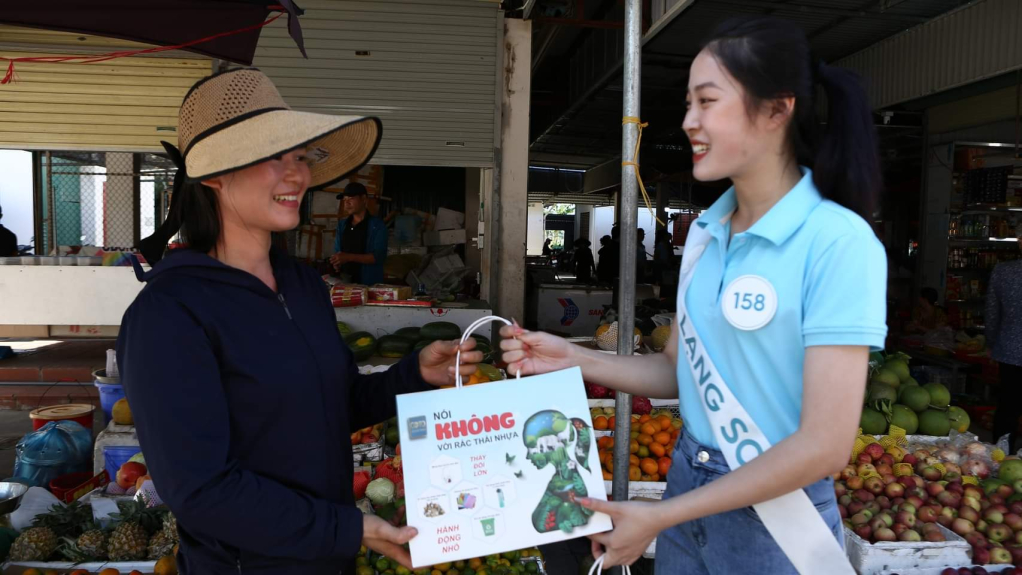 Thí sinh Cuộc thi Hoa hậu Biển đảo Việt Nam 2022 tặng túi giấy thân thiện với môi trường cho hộ dân kinh doanh.