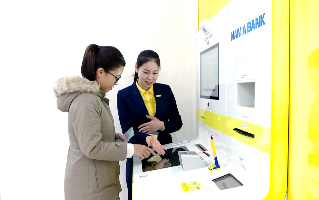 Nhân viên Ngân hàng Thương mại CP Nam Á hướng dẫn khách hàng rút tiền qua hệ thống máy rút tiền ATM. Ảnh: Mạnh Trường