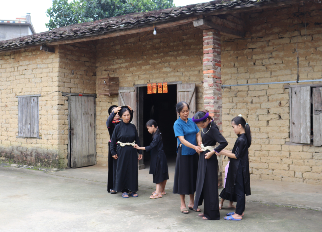 Người dân thôn Bản Cáu, xã Lục Hồn, huyện Bình Liêu chỉnh trang phục bên nếp nhà truyền thống. 